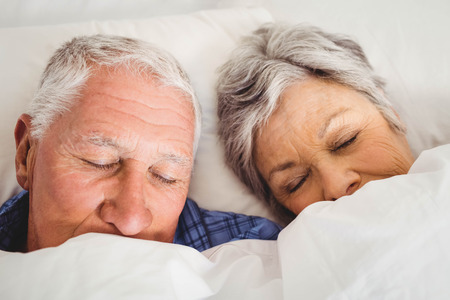 Senior couple sleeping on bed in bedroomの写真素材