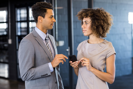 Businessman talking to young woman holding mobile phone in officeの写真素材