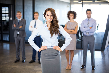 Successful businesswoman smiling at camera while her colleagues standing behind him in officeの写真素材