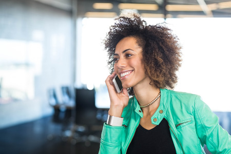 Close-up of young woman talking on mobile phone in front of conference room in the office