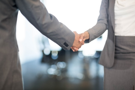 Close-up of businessman shaking hands with businesswoman in officeの写真素材