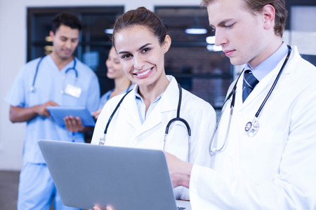 Doctors using laptop and smiling at camera while her colleagues discussing behindの写真素材