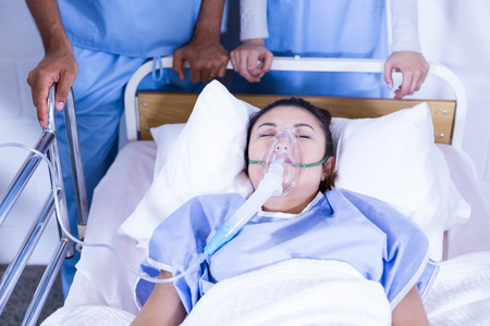 Patient with oxygen mask lying on bed and doctors standing near the bedの写真素材