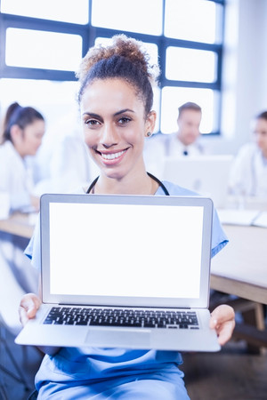 Portrait of female doctor showing laptop and other doctors discussing behind in conference roomの写真素材