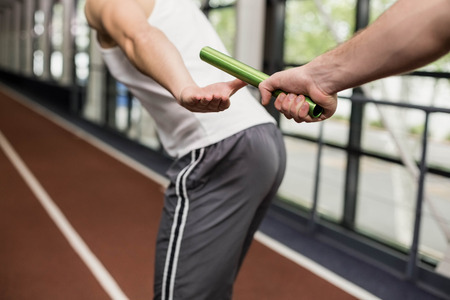 Man passing the baton to partner on track at the gymの写真素材