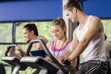 Trainer woman talking with a man doing exercise bike at gym