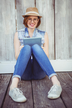 smiling hipster woman, sitting on the ground, holding a tablet computerの写真素材