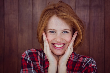 smiling hipster woman with her hands on her face against a wooden background