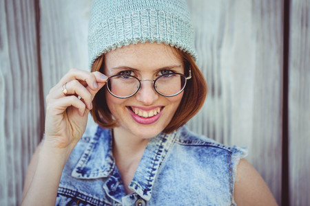 smiling hipster woman in a beanie and glasses against a wooden baackkgroundの写真素材