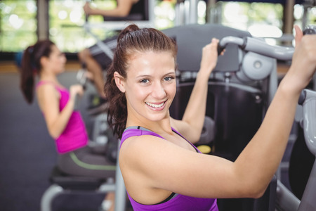 Fit woman using weight machine in gym