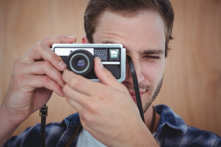 Handsome hipster taking picture with retro camera on a wooden backgroundの写真素材