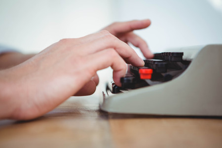 masculine hands typing on old typewriter on wooden table
