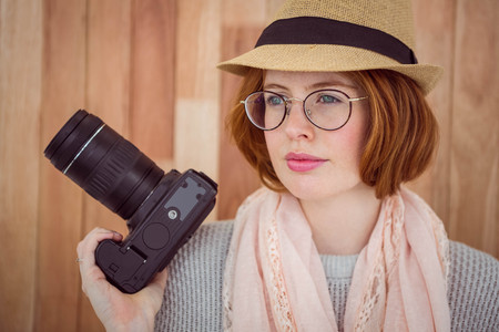 Hipster smiling and holding camera on wooden background