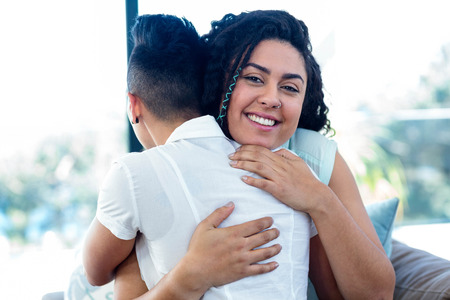 Lesbian couple embracing each other on sofa in living roomの写真素材