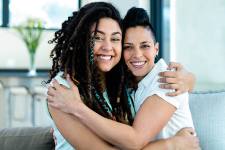 Portrait of happy lesbian couple embracing each other and smiling in living roomの写真素材