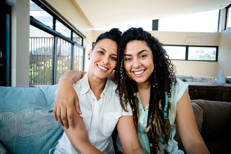 Portrait of happy lesbian couple embracing each other and smiling in living roomの写真素材