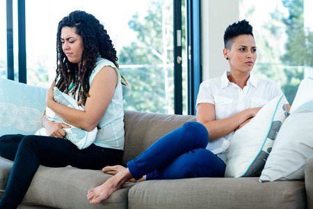 Unhappy lesbian couple sitting on sofa in living roomの写真素材