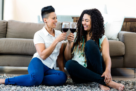 Lesbian couple sitting on rug and toasting wine glassesの写真素材