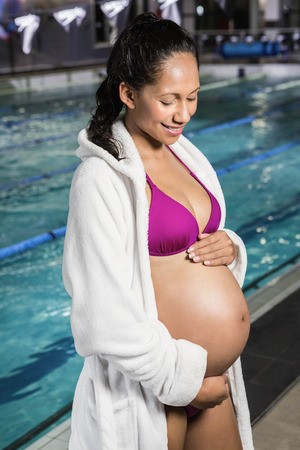 Pregnant woman touching her belly at the swimming poolの写真素材