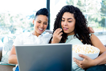 Lesbian couple having popcorn while using laptop in living roomの写真素材