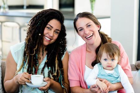 Portrait of two women smiling and sitting on sofa with a babyの写真素材