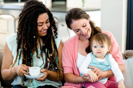 Two women smiling and sitting on sofa with a babyの写真素材