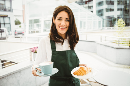 Waitress posing with coffee and croissant in cafeの写真素材