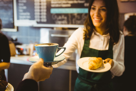 Waitress serving a cup of coffee in cafeの写真素材