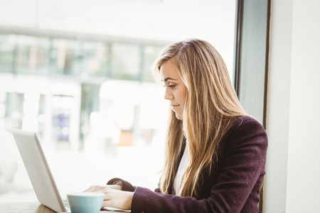 Cute blonde girl using her laptop in a coffee shop