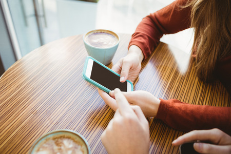 Friends using smartphone and having coffee in a coffee shopの写真素材