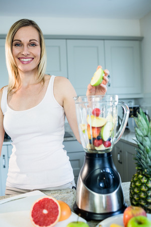 Pretty blonde woman preparing a smoothie with recipe on laptop in the kitchenの写真素材