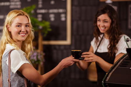 Pretty waitress giving cup of coffee to customer at coffee shopの写真素材