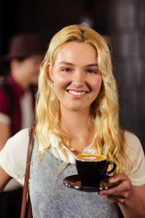 Portrait of smiling pretty customer holding cup of coffee at coffee shopの写真素材