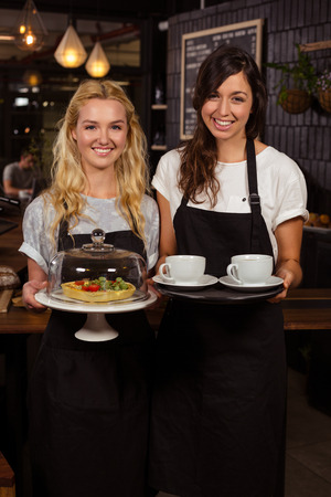 Pretty waitresses posing in front of the counter presenting coffee and pie at the coffee shopの写真素材