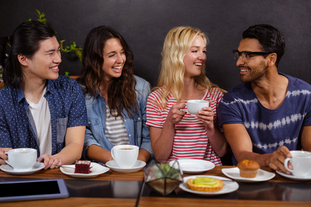 Smiling friends enjoying coffee together and using technologies at the coffee shopの写真素材