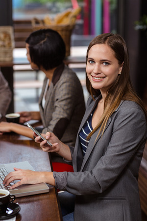 Smiling woman using smartphone in a cafeの写真素材