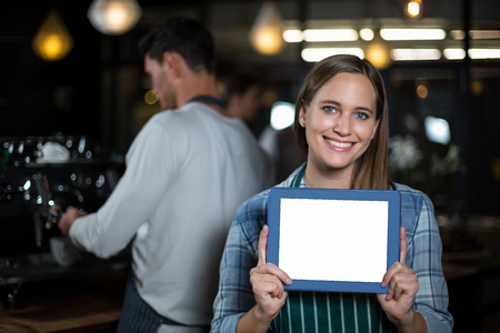 Pretty barista showing tablet screen at the camera in the barの写真素材