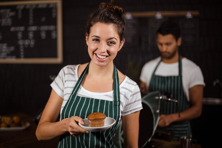 Smiling barista holding muffin in the barの写真素材
