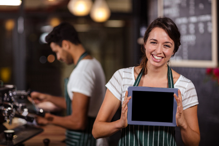 Smiling barista showing tablet at the camera in the barの写真素材