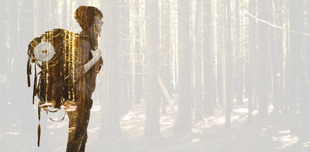 Side view of a hipster woman with a travel bag against trees in a woodsの写真素材