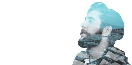 Close-up of thoughtful hipster looking away against majestic shot of trees and mountain range against cloudscapeの写真素材