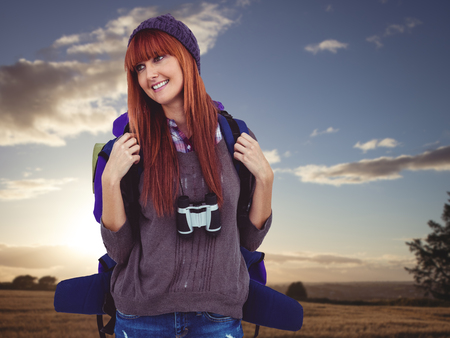Smiling hipster woman with a travel bag against sunset over a fieldの写真素材