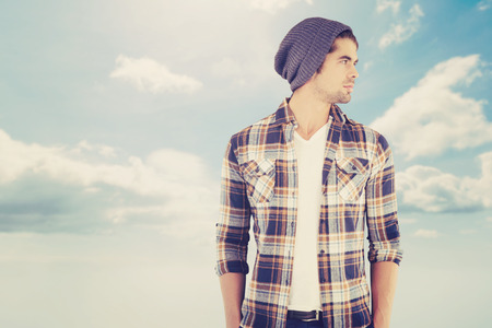 Confident hipster looking away while standing against blue skyの写真素材