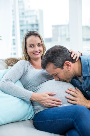 Man sitting on sofa and kissing pregnant womans stomachの写真素材