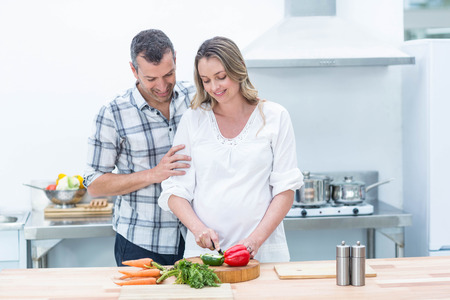 Pregnant woman busy in kitchen cutting vegetablesの写真素材