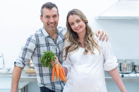 Portrait of pregnant woman looking at camera while holding carrotsの写真素材