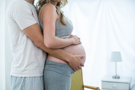 Man holding pregnant womans stomach in bedroomの写真素材