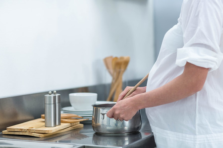 Pregnant woman busy in kitchen preparing foodの写真素材