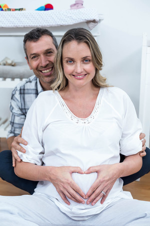 Couple making a heart shape on the pregnant belly with their handsの写真素材