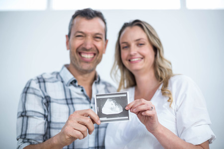 Portrait of pregnant couple holding sonography report at homeの写真素材